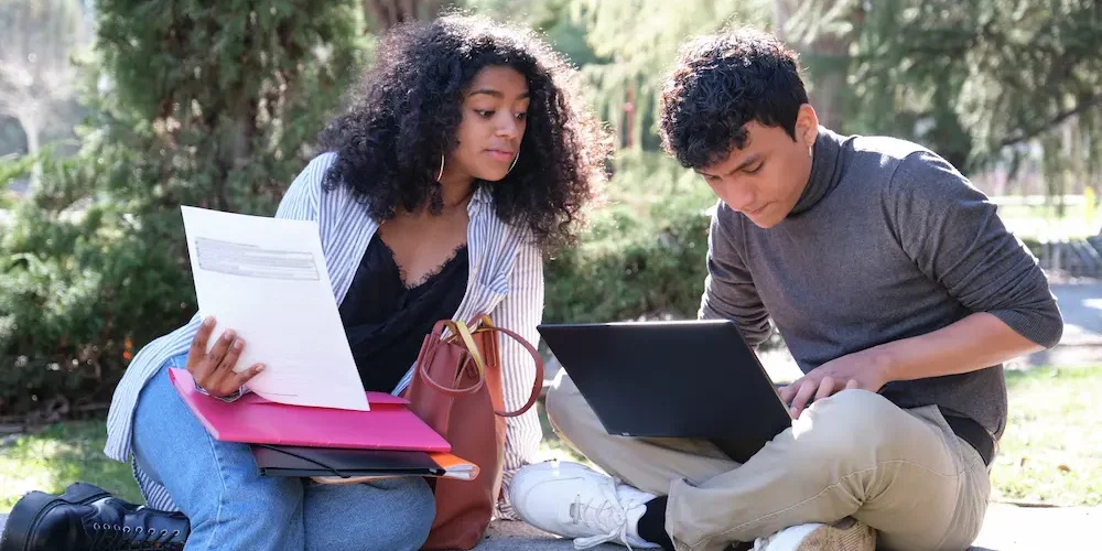 Two latin students studying together sitting on a bench outdoors