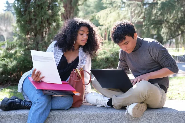 Two latin students studying together sitting on a bench outdoors